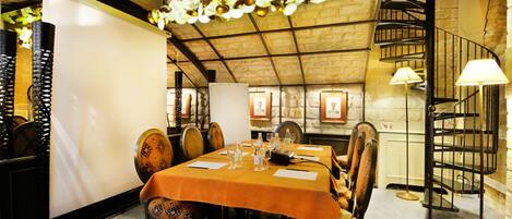 Een restaurant met een lange eettafel, een spiltrap en een hangende plantdecoratie.