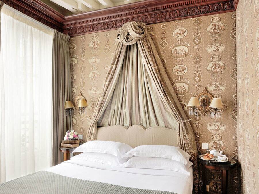 Un dormitorio con cama a dosel, papel tapiz decorativo y una lámpara de araña clásica.