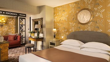 Une chambre d’hôtel avec un grand lit, un canapé rouge, une petite table avec une lampe et un mur recouvert d’un papier peint à motifs floraux.