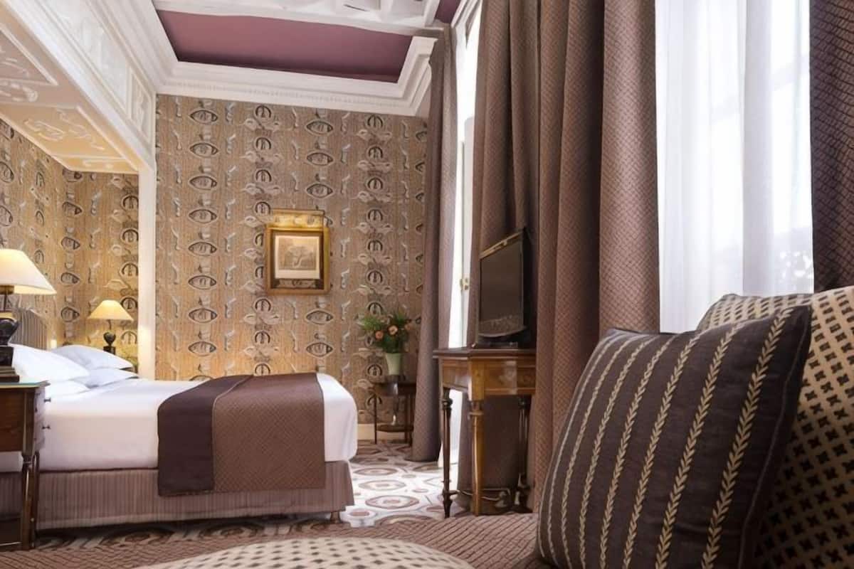 Ein Hotelzimmer mit Bett, Fernseher, Schreibtisch und strukturierter Wandtapete.