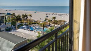 A beach view from a balcony with a pool, palm trees, and beach chairs. - St Pete Shores Hotel (St. Pete Beach)