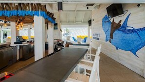 A restaurant with a long counter, white chairs, and a mural of a fish on the wall. - St Pete Shores Hotel (St. Pete Beach)