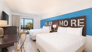 A hotel room with two beds, a desk, a chair, and a large window with a view of the ocean. - St Pete Shores Hotel (St. Pete Beach)