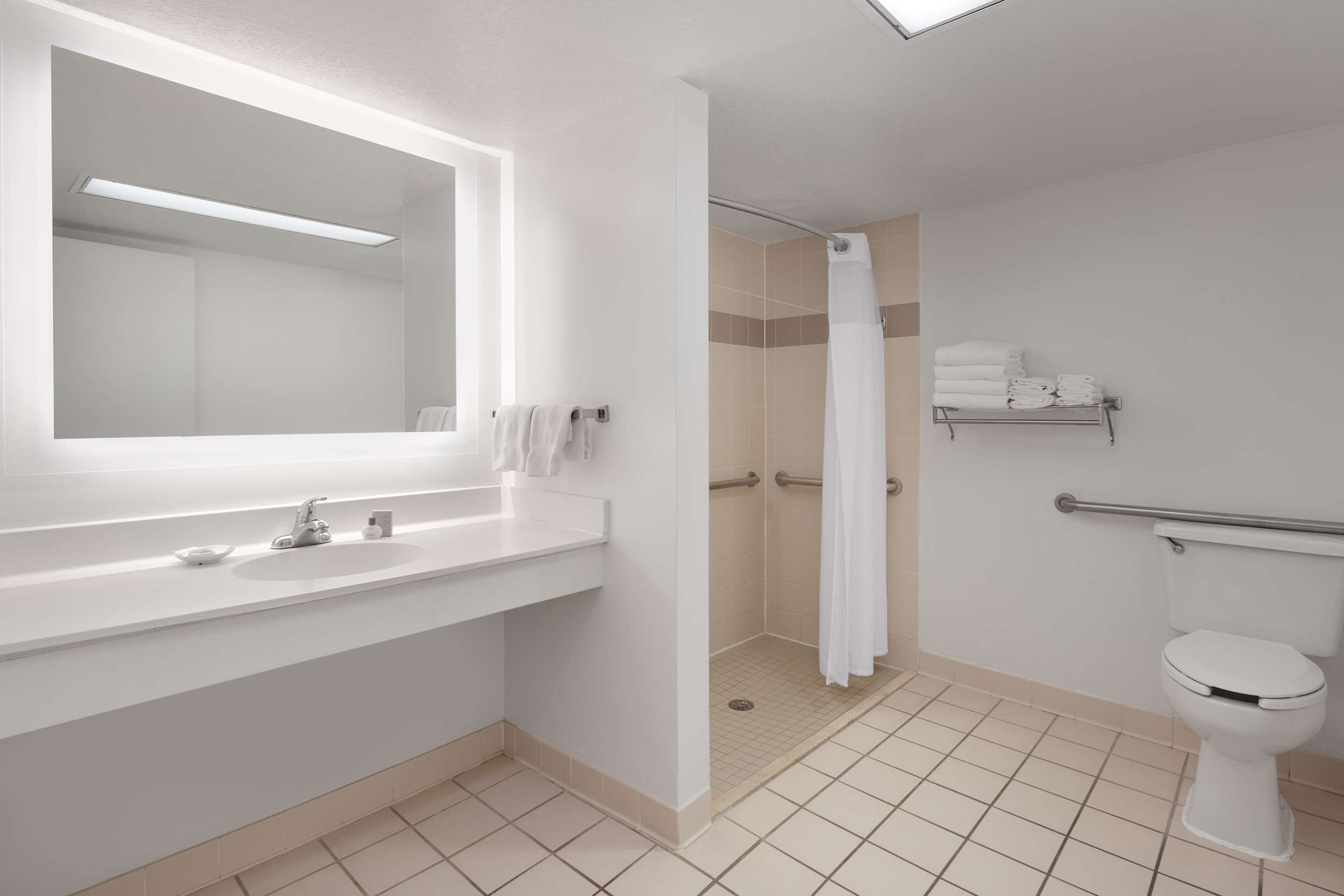 A modern bathroom with a large mirror, white sink, and a shower with a white curtain.