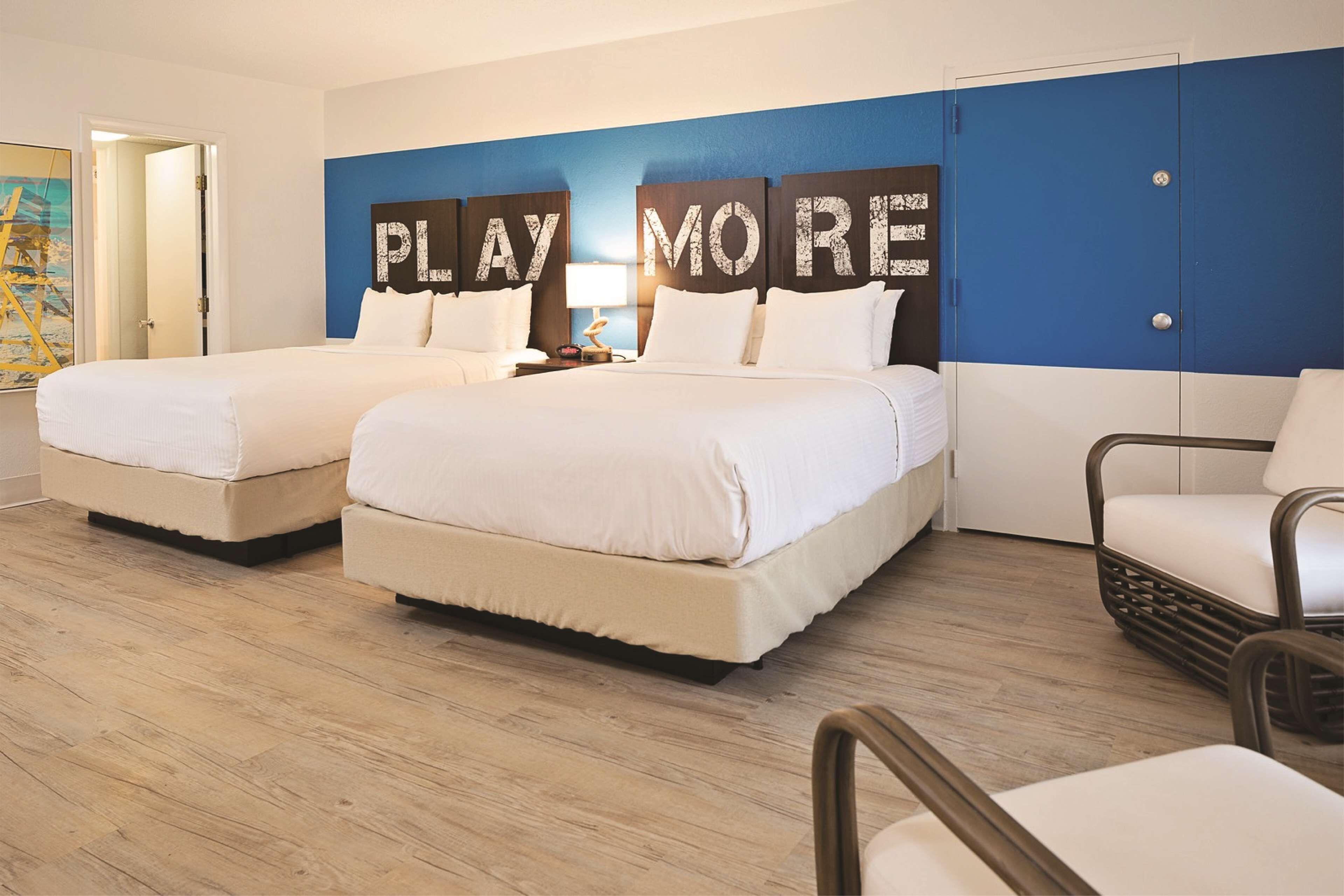 A hotel room with two beds, a blue accent wall, and a wooden floor.