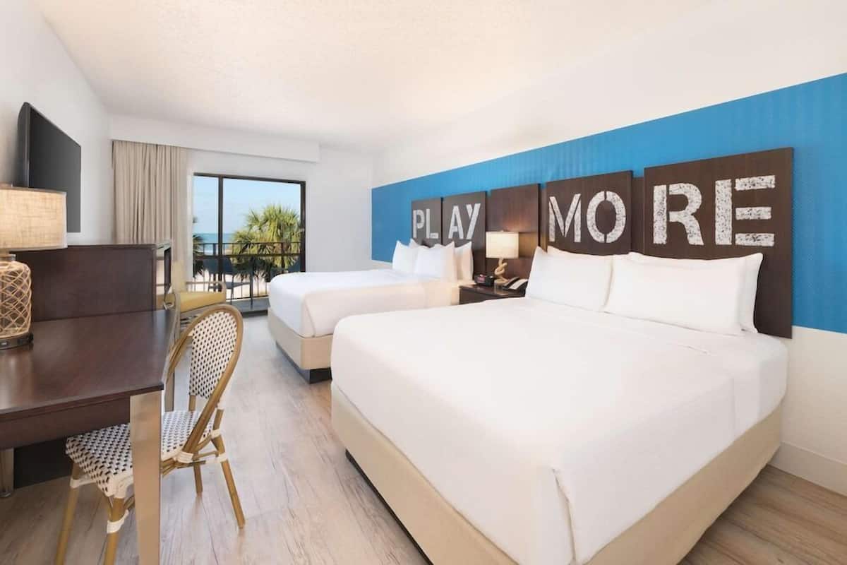 A hotel room with two beds, a desk, a chair, and a large window with a view.