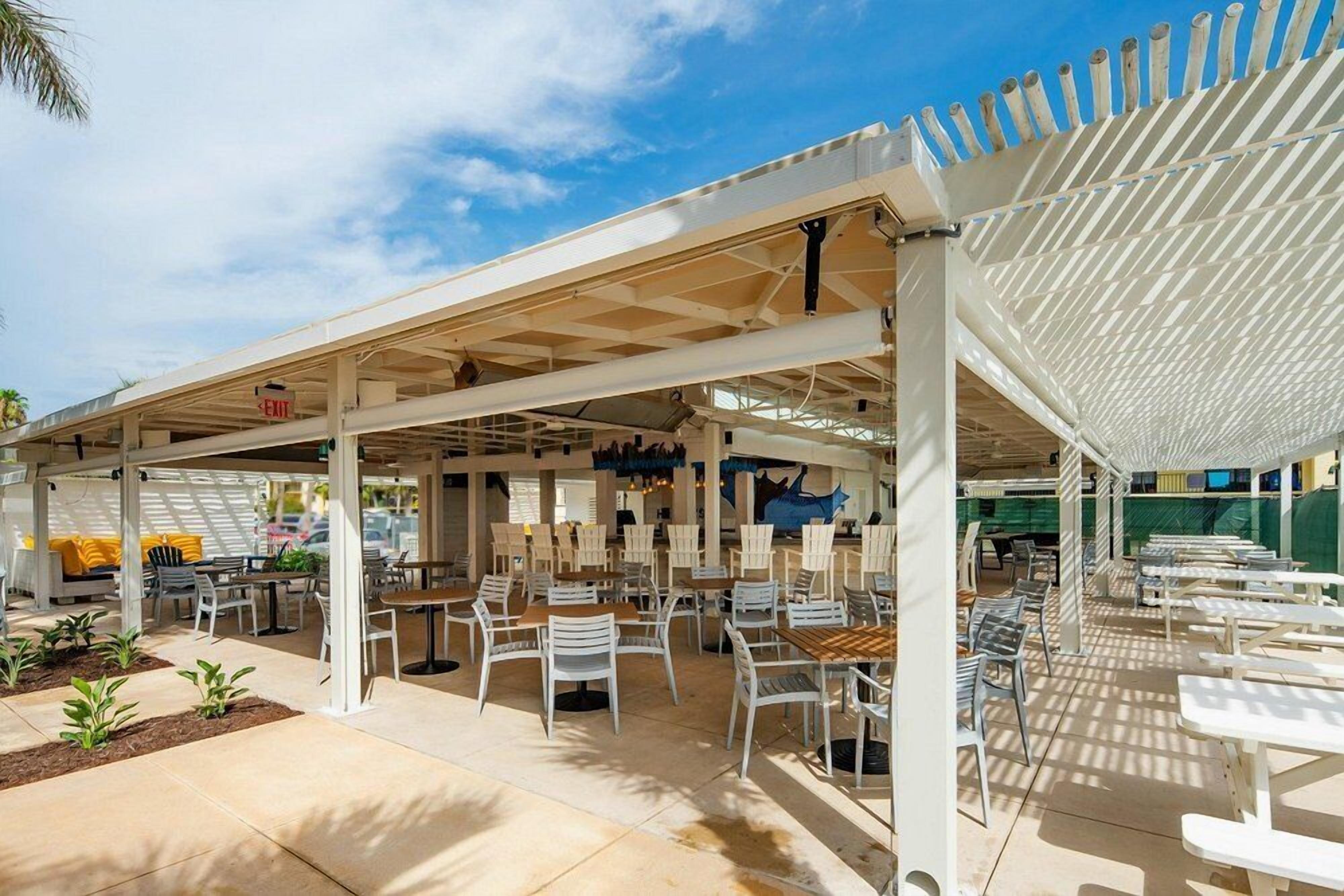 An outdoor patio area with tables and chairs, covered by a white pergola, and a sign indicating an exit.