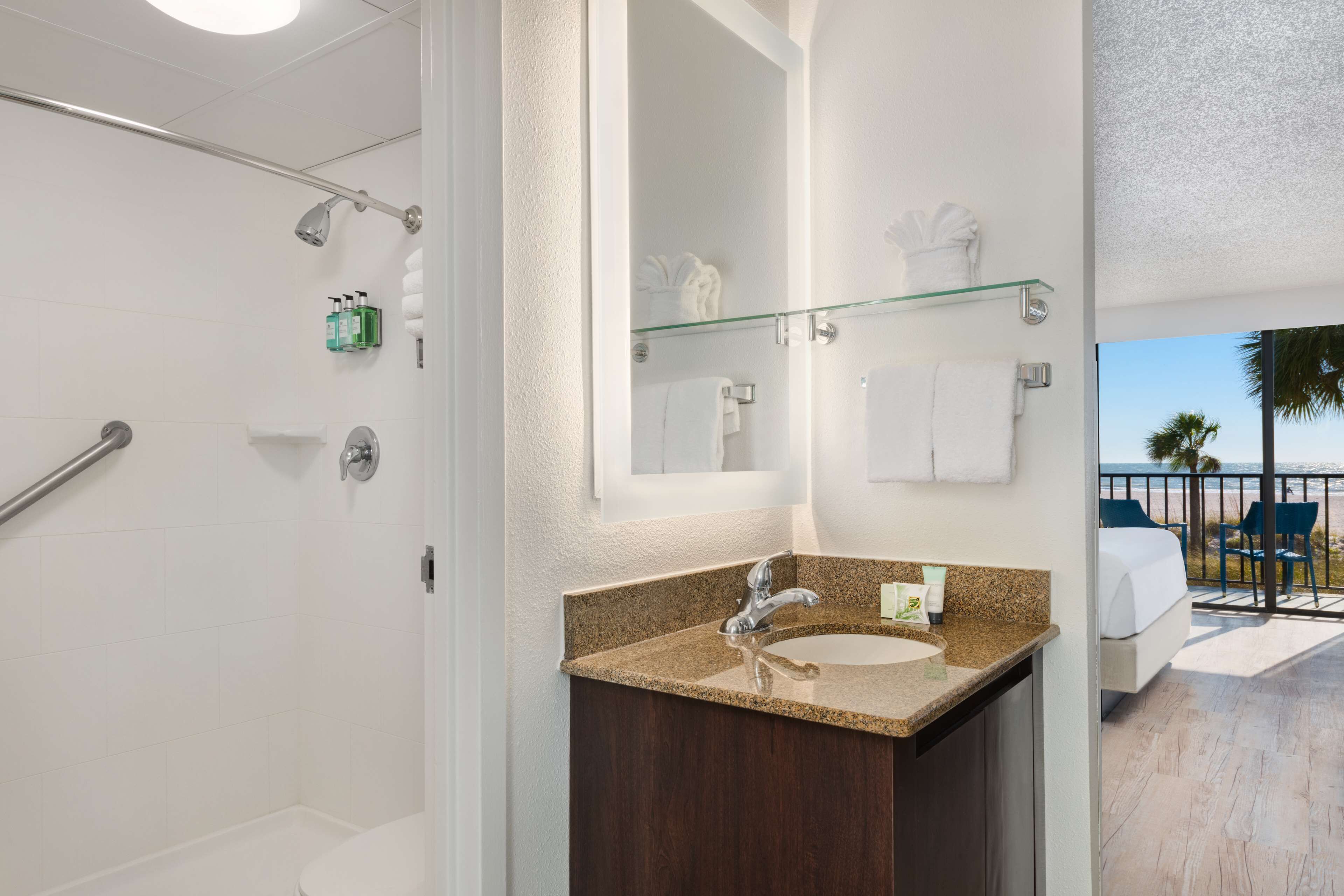 A bathroom with a glass shower enclosure, a sink with a granite countertop, and a large mirror.