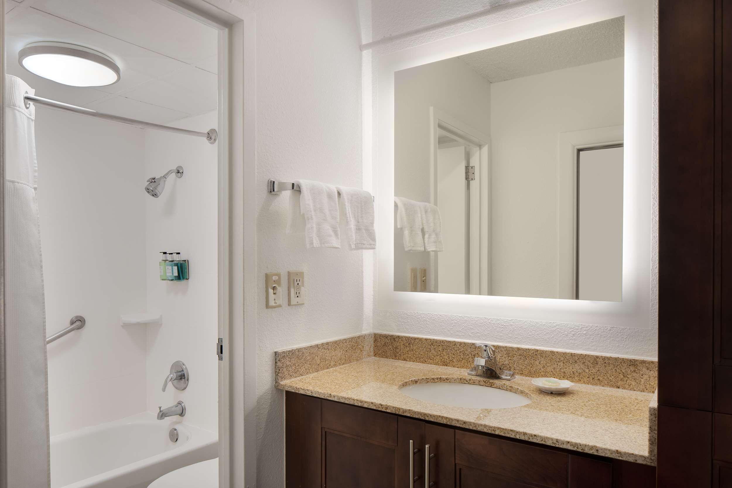 A bathroom with a white shower, a sink with a granite countertop, and a large mirror above the sink.