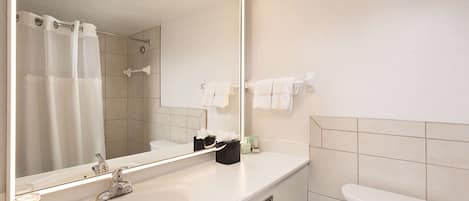 A bathroom with a large mirror, a sink, a toilet, and a shower curtain.