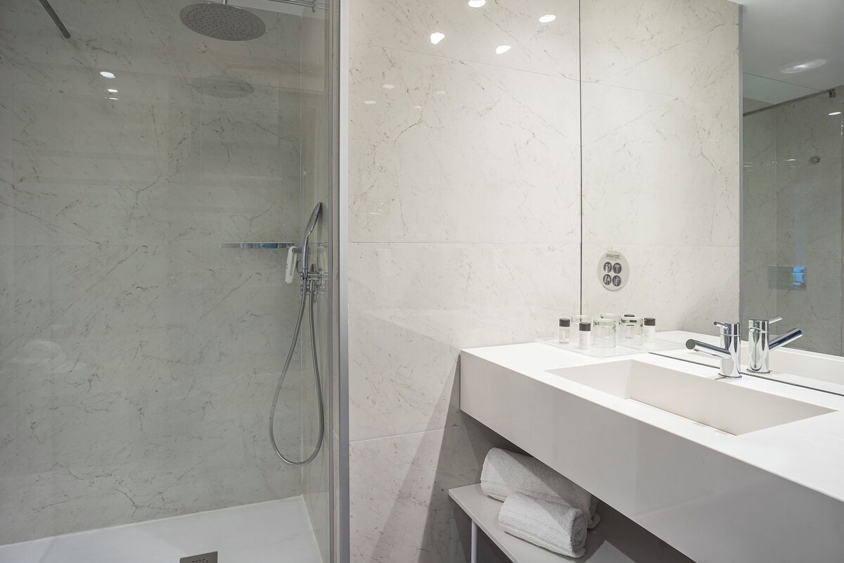 A modern bathroom with a glass-enclosed shower, a white sink, and a large mirror.