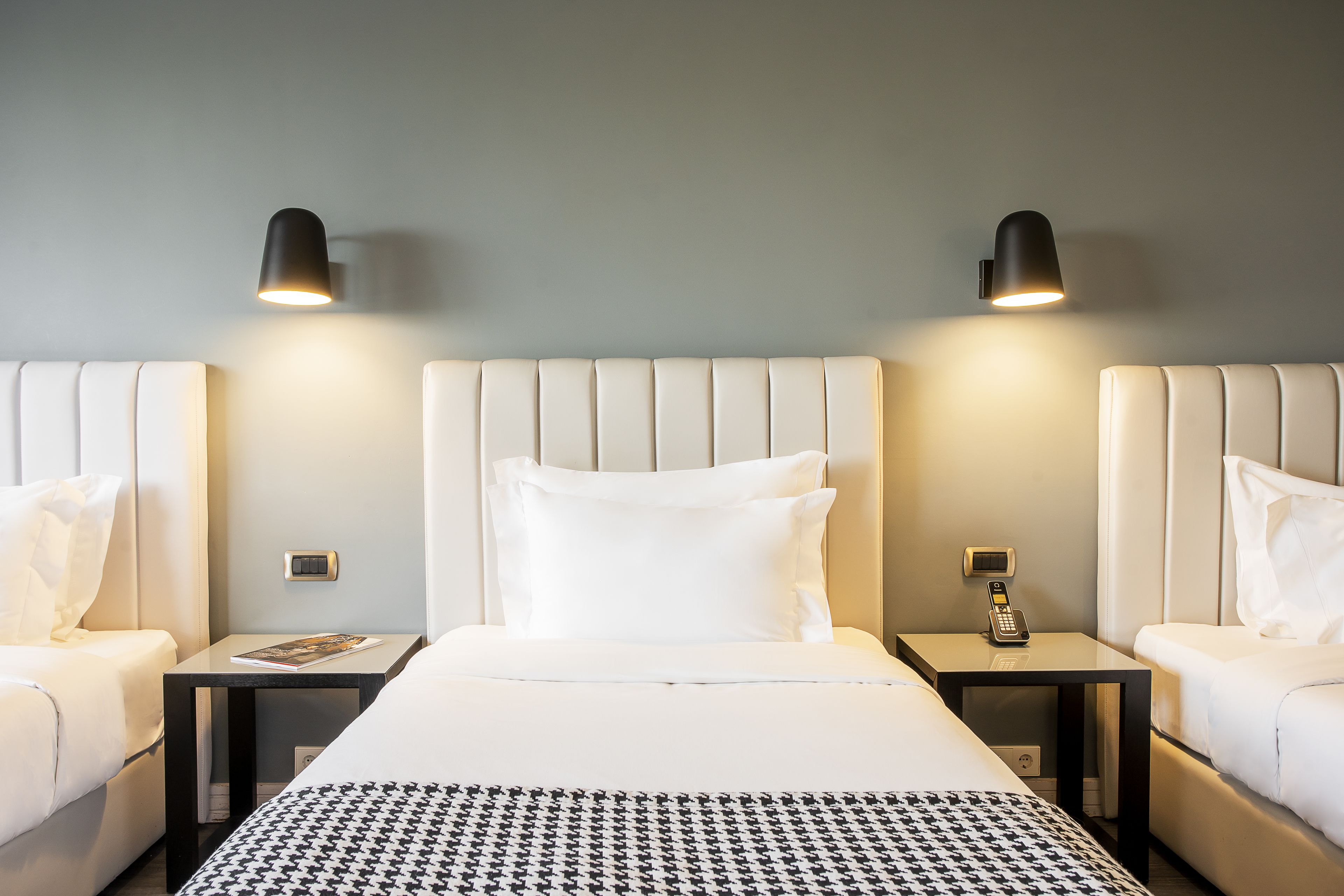 Quarto de hotel com cama grande, duas mesas de cabeceira, telefone fixado na parede e duas luminárias de parede.