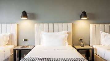 Quarto de hotel com cama grande, duas mesas de cabeceira, telefone fixado na parede e duas luminárias de parede.