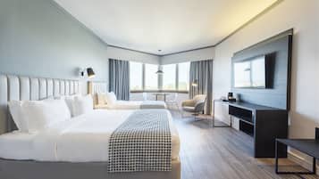 Quarto de hotel moderno com uma cama grande, uma escrivaninha, uma cadeira e uma TV na parede.