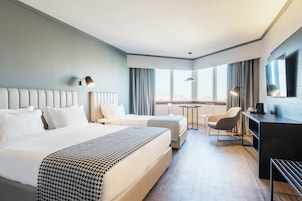 Quarto de hotel com uma cama grande, uma mesa, uma cadeira e uma televisão.