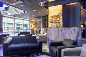 Una hall moderna con zone relax, un'ampia finestra vista città e una parete decorativa con un quadro incorniciato.