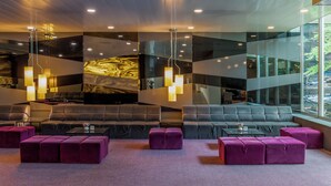 A modern lounge area with a large sectional sofa, purple ottomans, and pendant lighting. - HF Ipanema Porto (Porto)