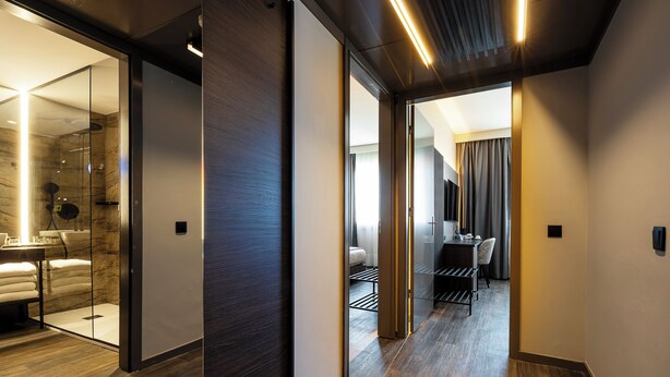 A modern hotel interior with a hallway leading to a bathroom with a glass shower enclosure and a visible bed. - HF Ipanema Porto (Porto)