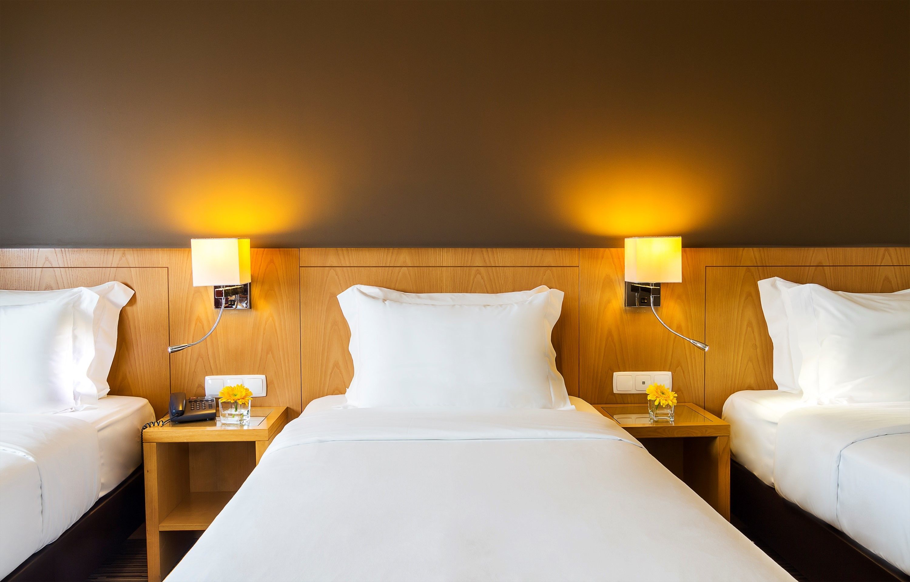 Quarto de hotel com uma cama grande, duas mesinhas de cabeceira e duas luminárias fixadas na parede.