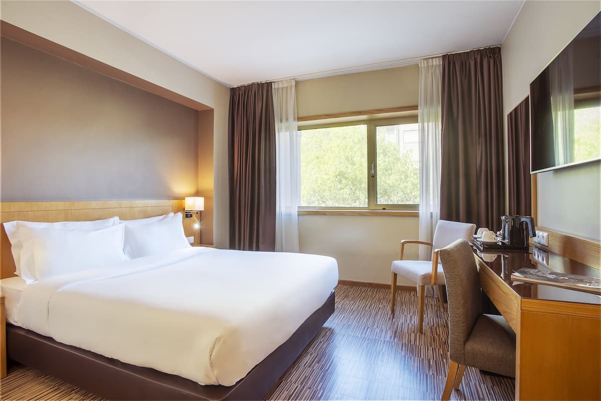 A hotel room with a large bed, a desk, a chair, and a window with curtains.