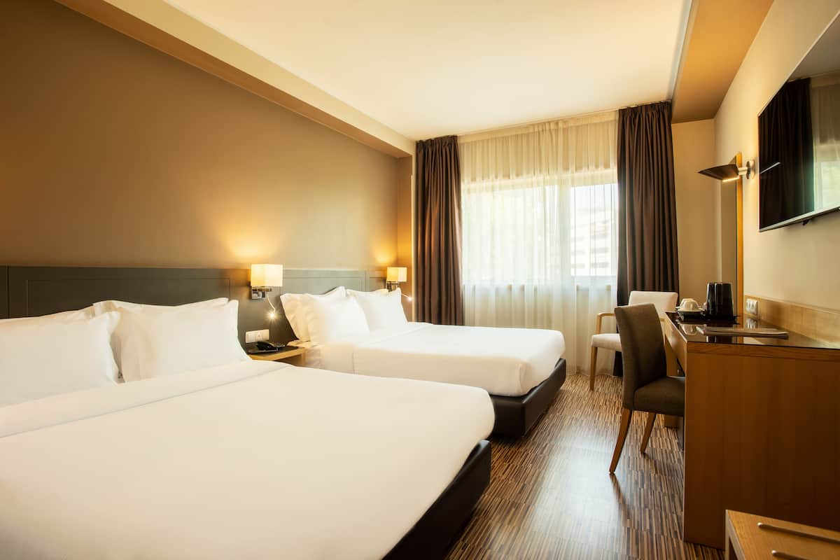 A hotel room with two beds, a desk, a chair, and a TV mounted on the wall.