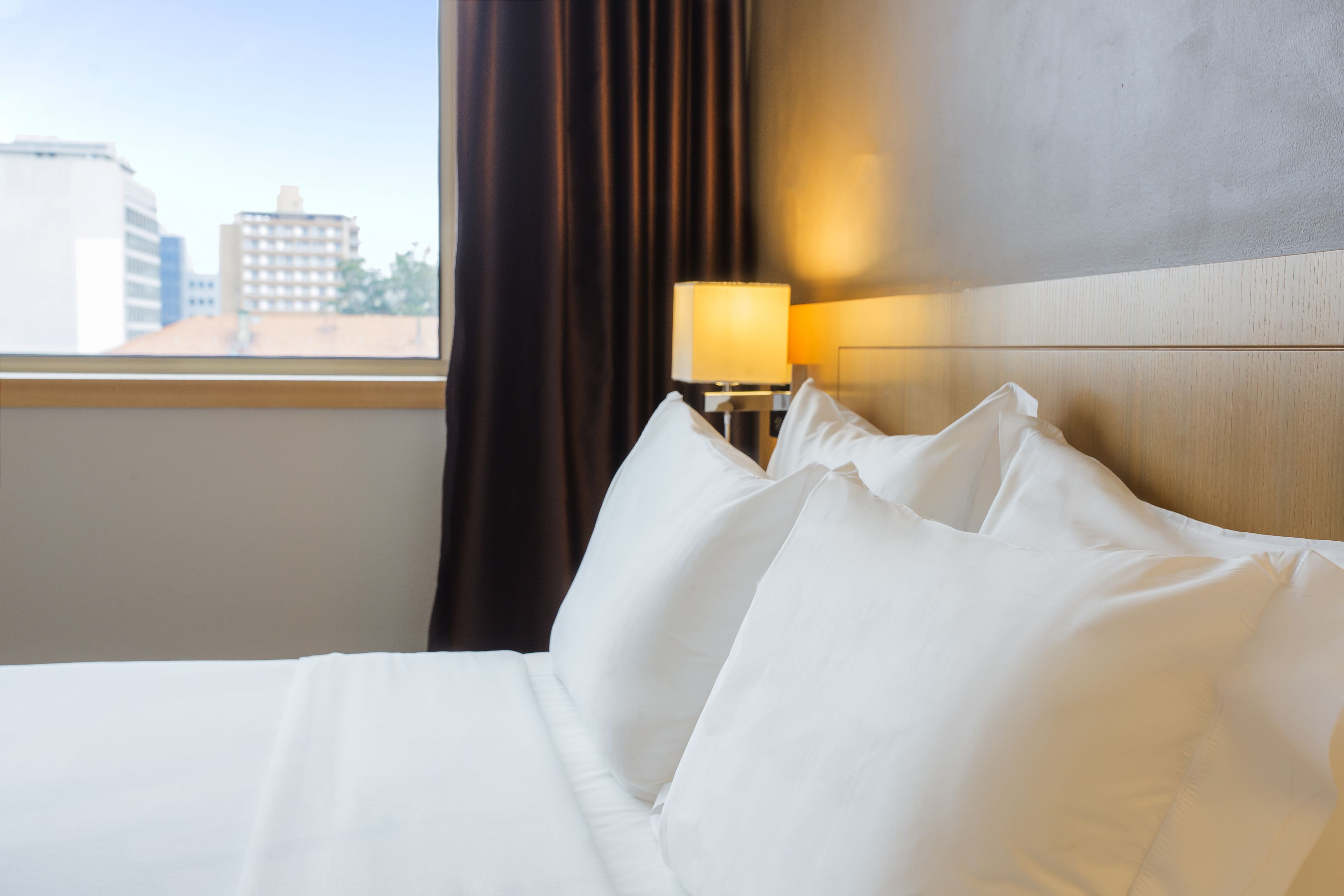 Une chambre d’hôtel avec un lit soigneusement fait, une lampe sur la table de chevet et une vue sur les immeubles par la fenêtre.