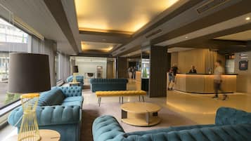 En modern entréhall med bekväma, blå soffor, en receptionsdisk och ett stort fönster med utsikt över gatan.
