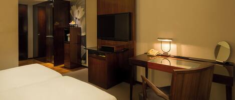Quarto de hotel com uma cama, uma escrivaninha com telefone, uma televisão e um espelho.