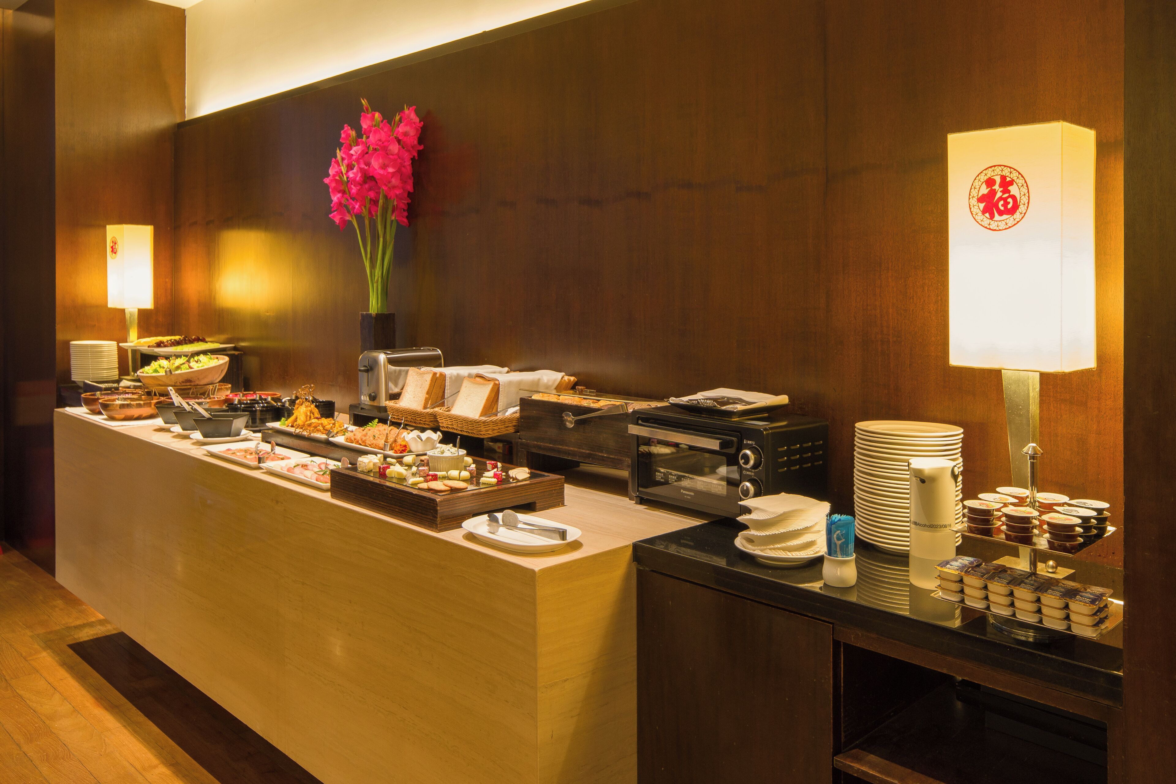A buffet setup with various food items, a coffee machine, and a decorative vase with flowers.