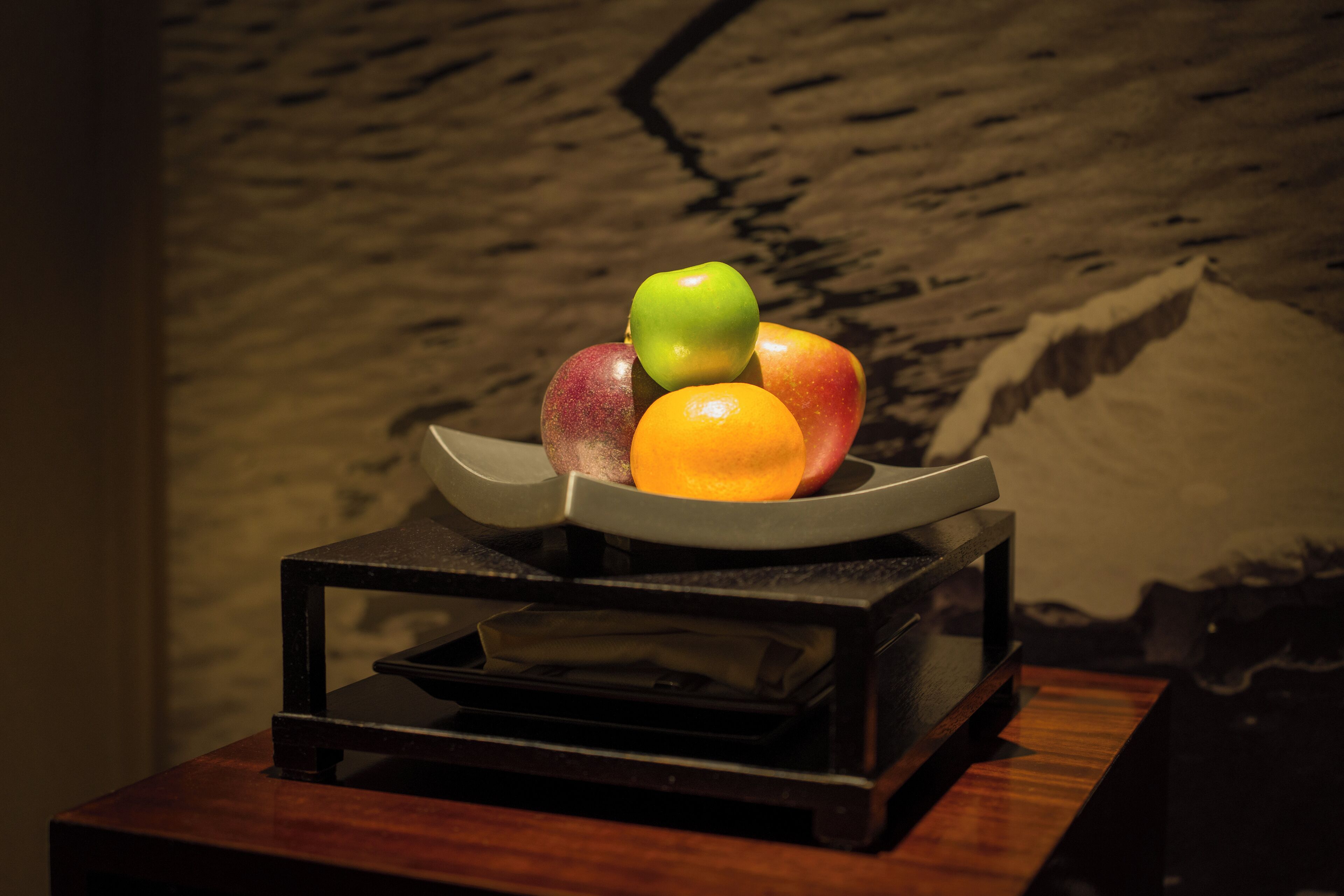A fruit bowl on a wooden table with a stone wall background.