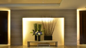Una moderna área de recepción con un banco, dos jarrones con flores y plantas decorativas altas.