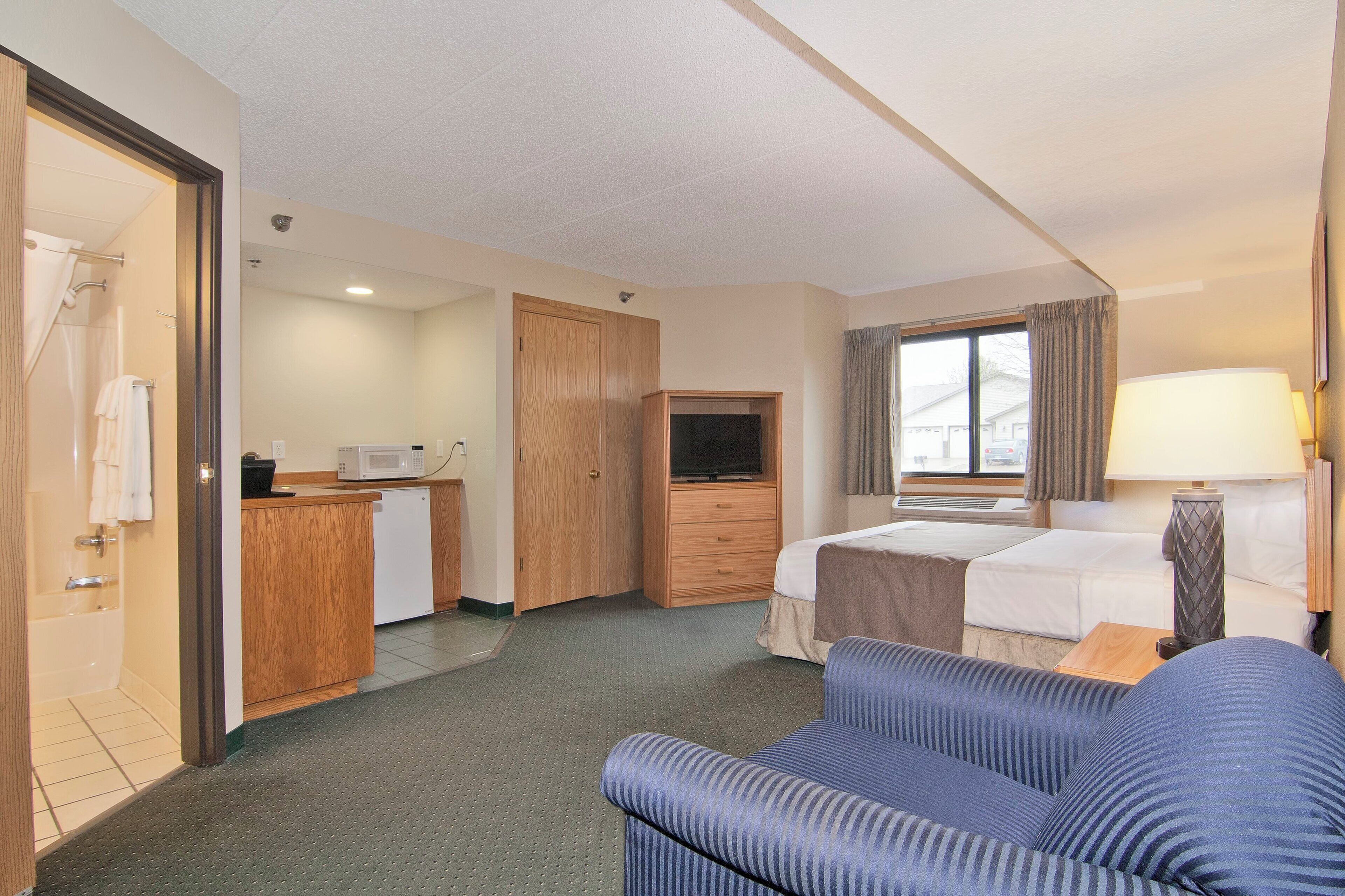 A hotel room with a kitchenette, a bed, a sofa, and a TV.