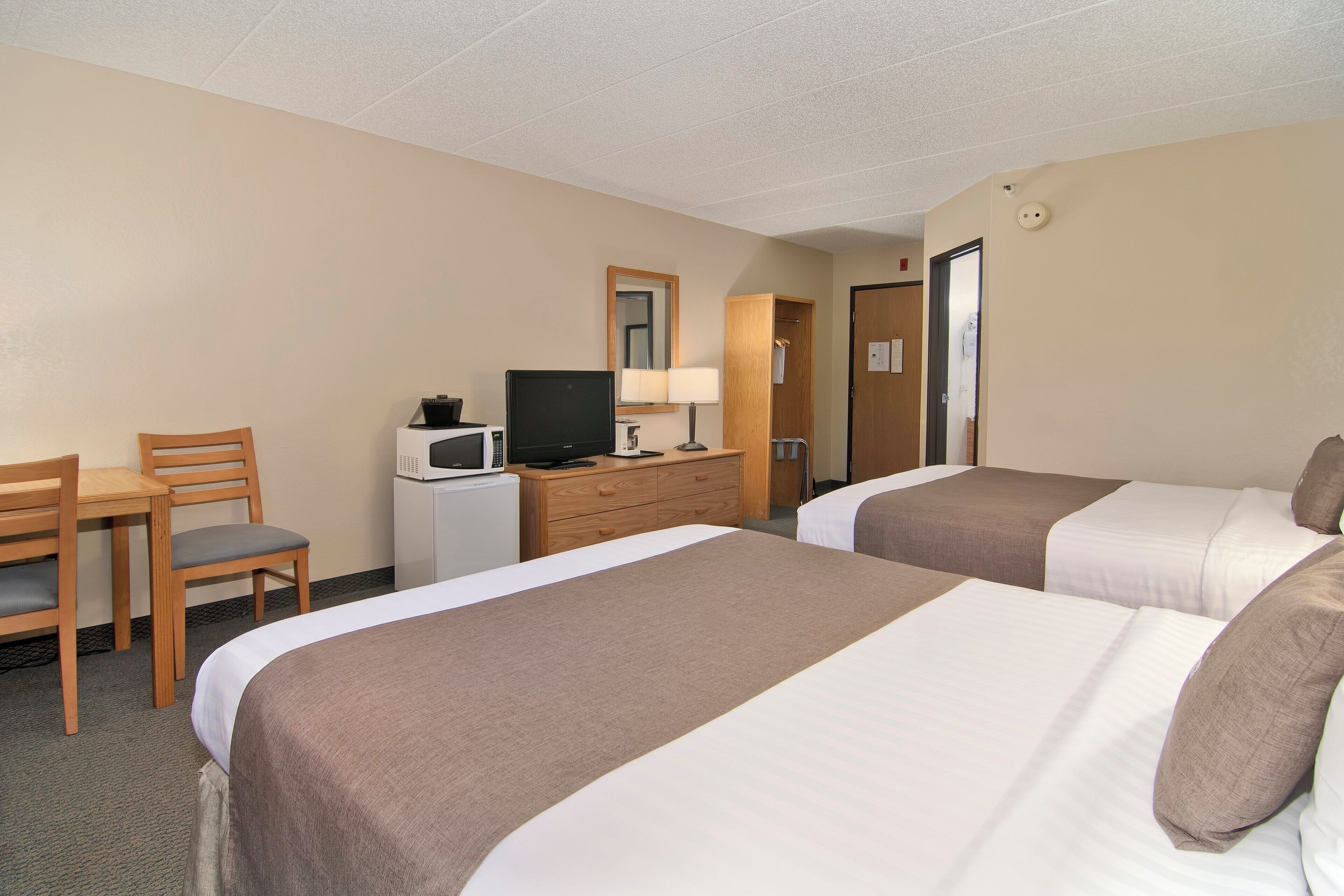 A hotel room with two beds, a desk with a chair, a television, and a dresser.