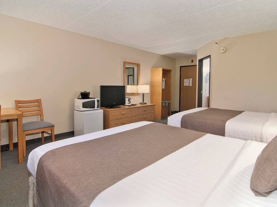 A hotel room with two beds, a desk with a chair, a television, and a dresser.