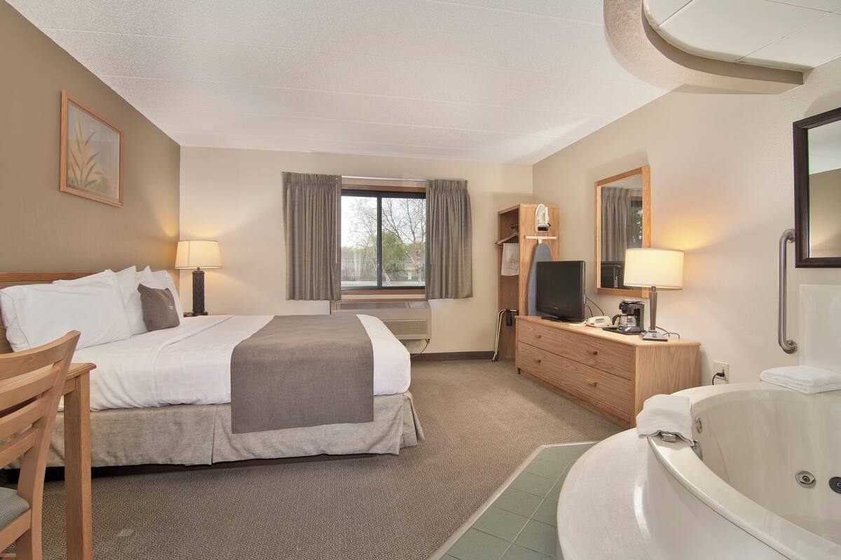 Een hotelkamer met een bed, een bureau, een televisie, een badkamer met bad en een raam met gordijnen.
