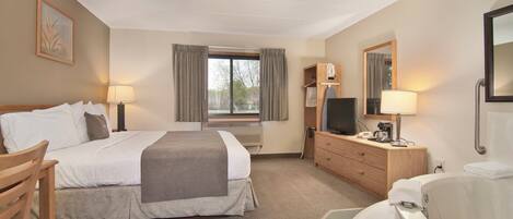 A hotel room with a bed, a desk, a TV, a bathroom with a bathtub, and a window with curtains.
