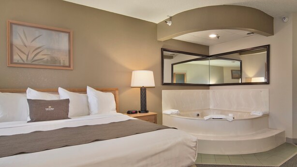 Habitación de hotel con una cama grande, una zona de estar con una silla y una mesa, una bañera y un espejo.