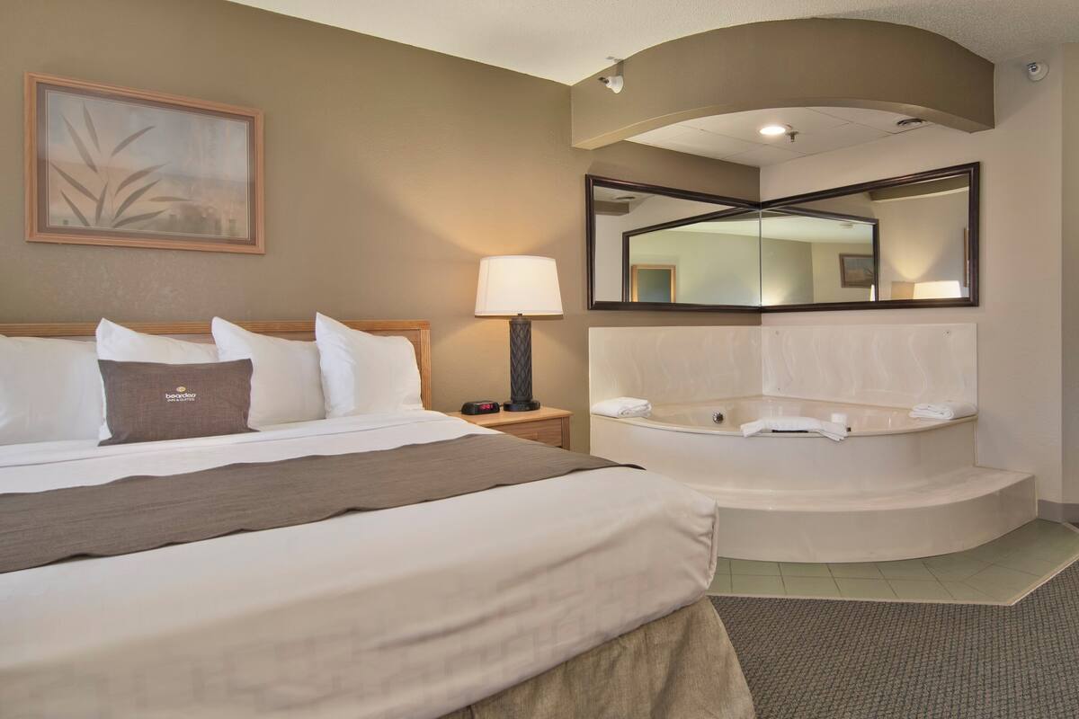 Hotelkamer met een groot bed, een zithoek met een stoel en een tafel, een badkuip en een spiegel.