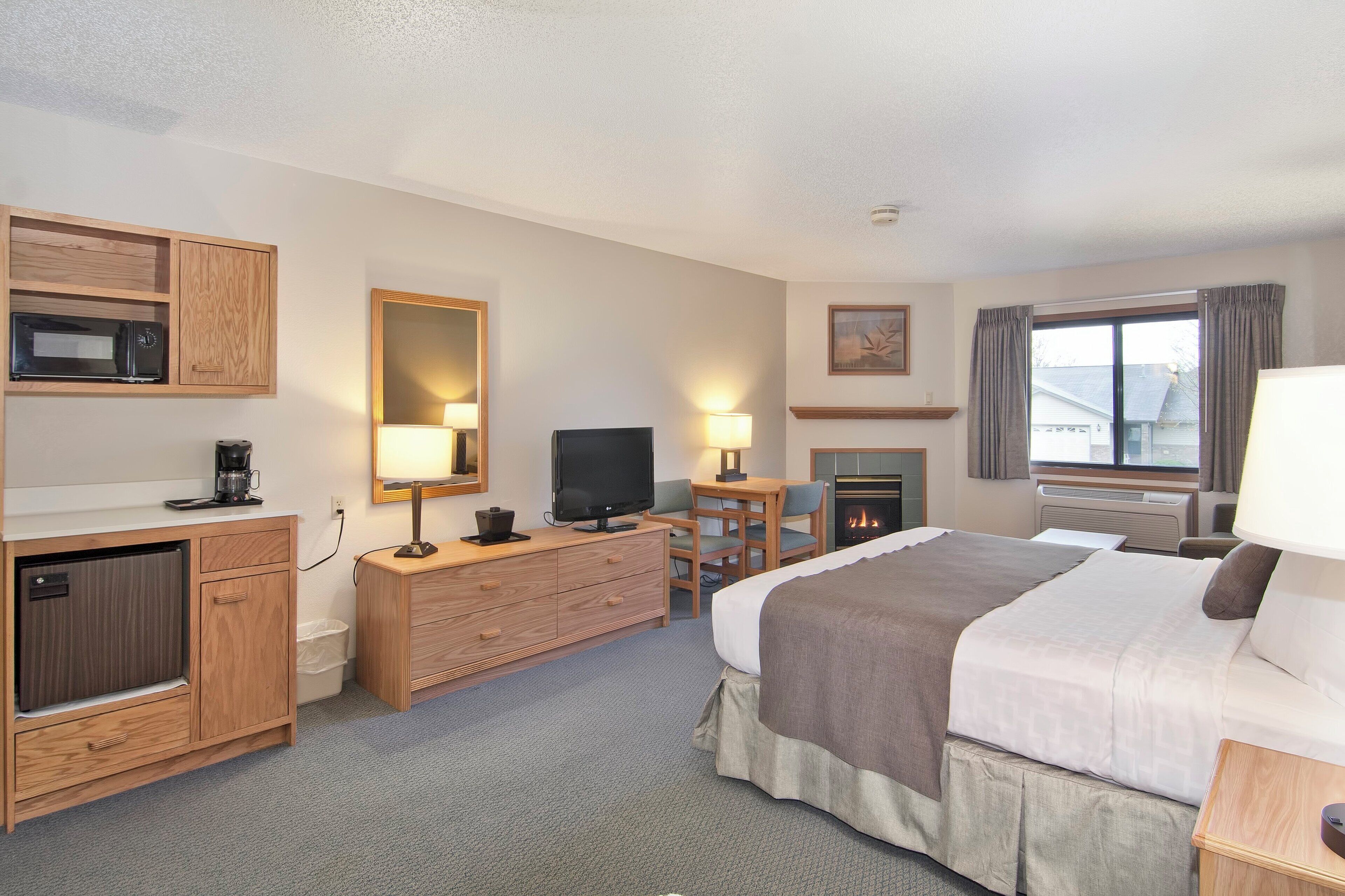 A hotel room with a bed, a television, a desk with a chair, a microwave, a coffee maker, and a fireplace.