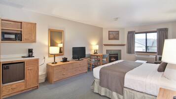 A hotel room with a bed, a television, a desk with a chair, a microwave, a coffee maker, and a fireplace.