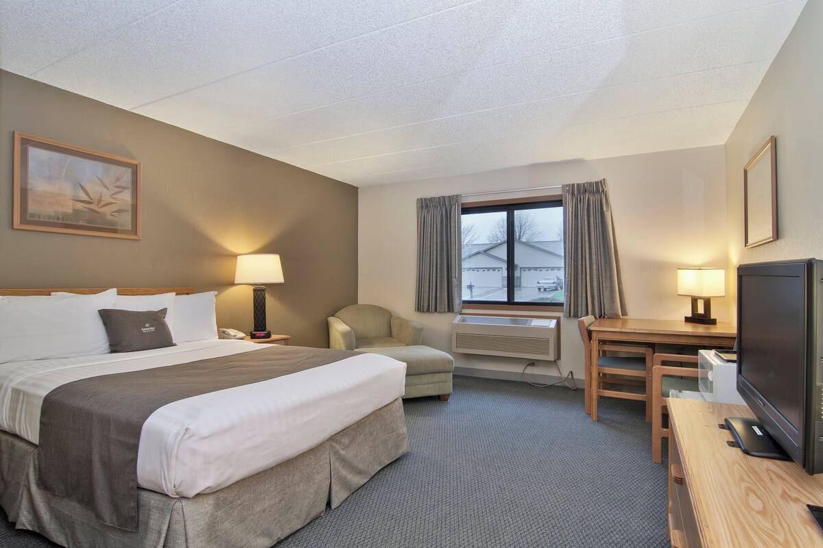 Een hotelkamer met een groot bed, een bureau met een televisie, een stoel en een raam met gordijnen.