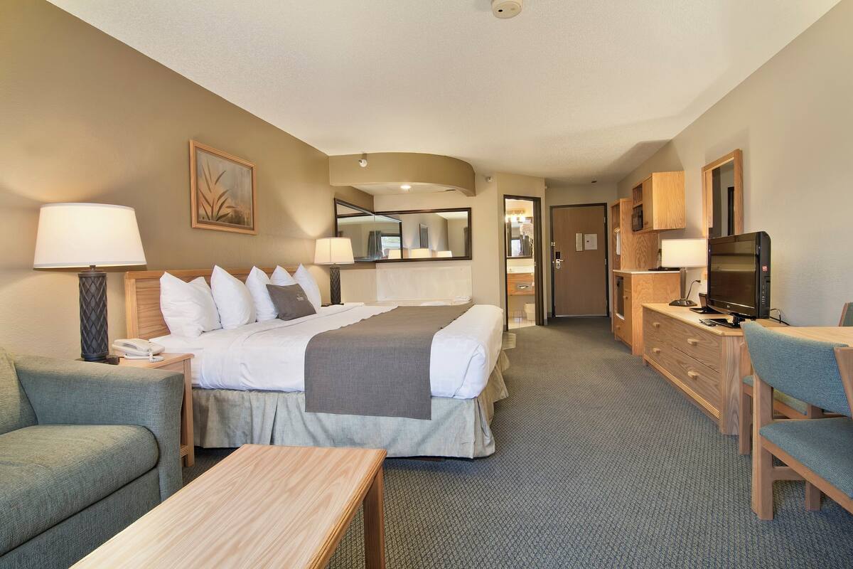 Een hotelkamer met een bed, een bureau, een stoel, een lamp, een televisie en een dressoir.