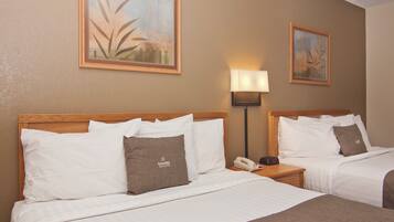 Habitación de hotel con dos camas, cada una con ropa blanca y almohadas marrones, una mesita de noche con lámpara y cuadros en las paredes.