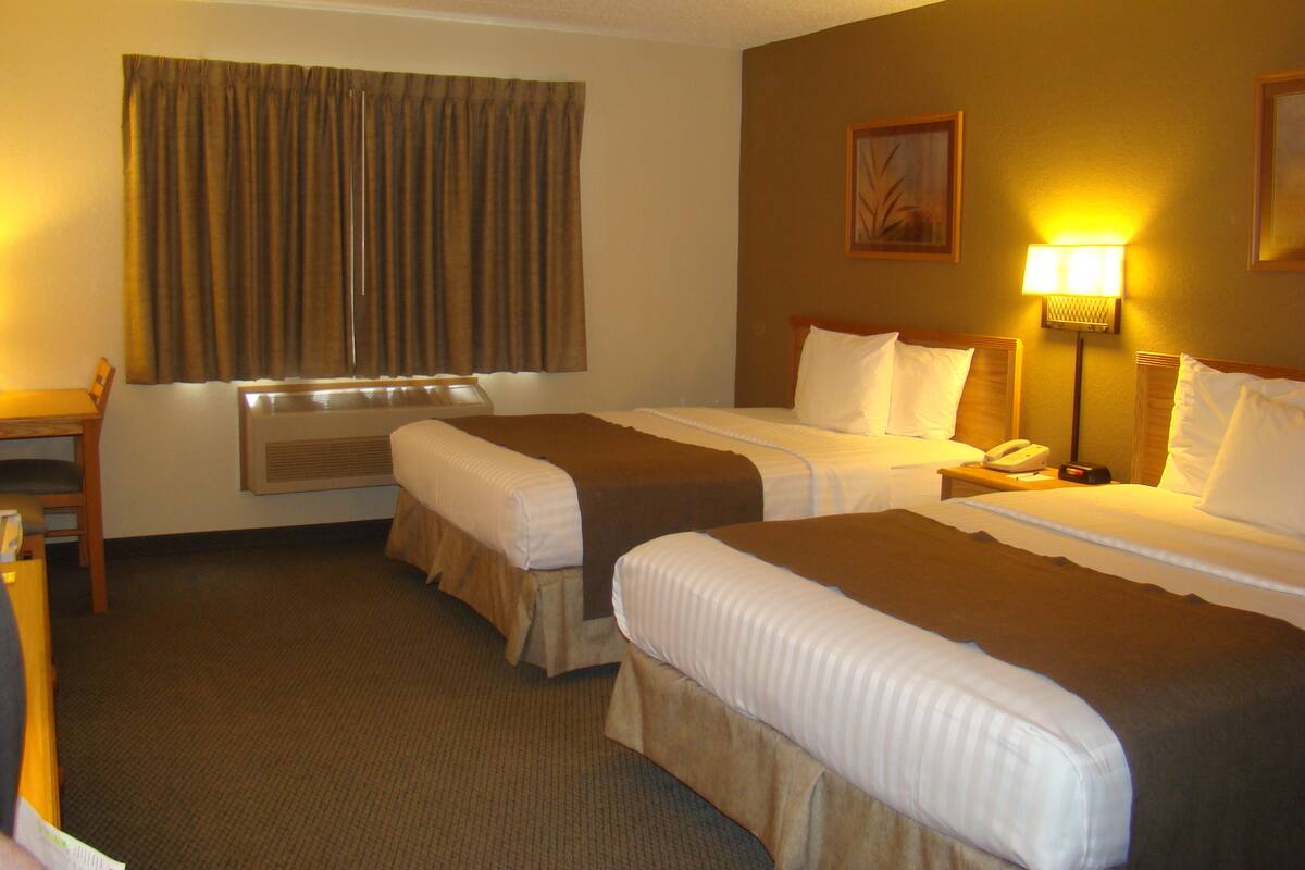 Een hotelkamer met twee bedden, een bureau, een stoel, een lamp en een raam met gordijnen.