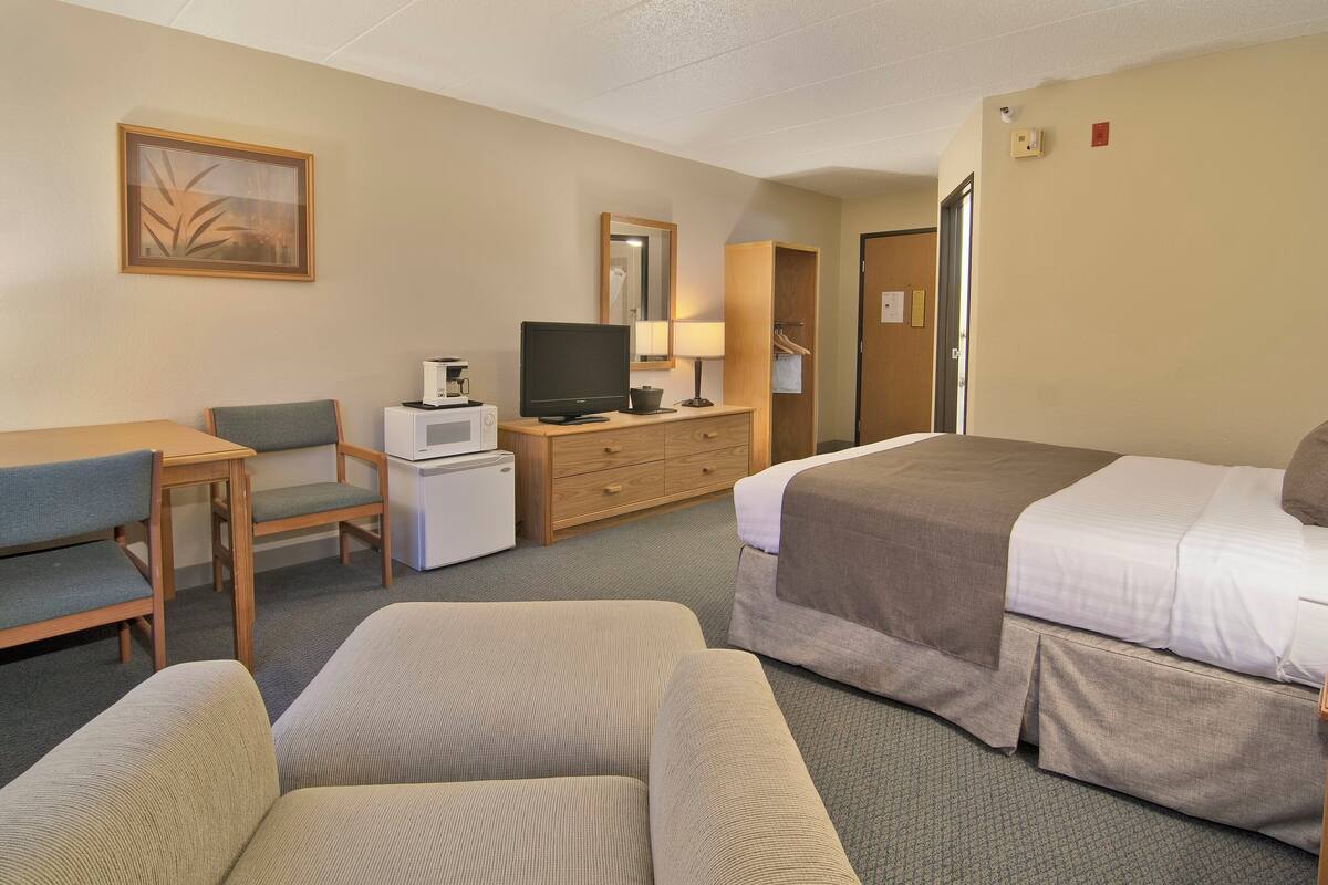 Hotelkamer met een bed, twee fauteuils, een bureau met een computer, een televisie, een kast en een spiegel.