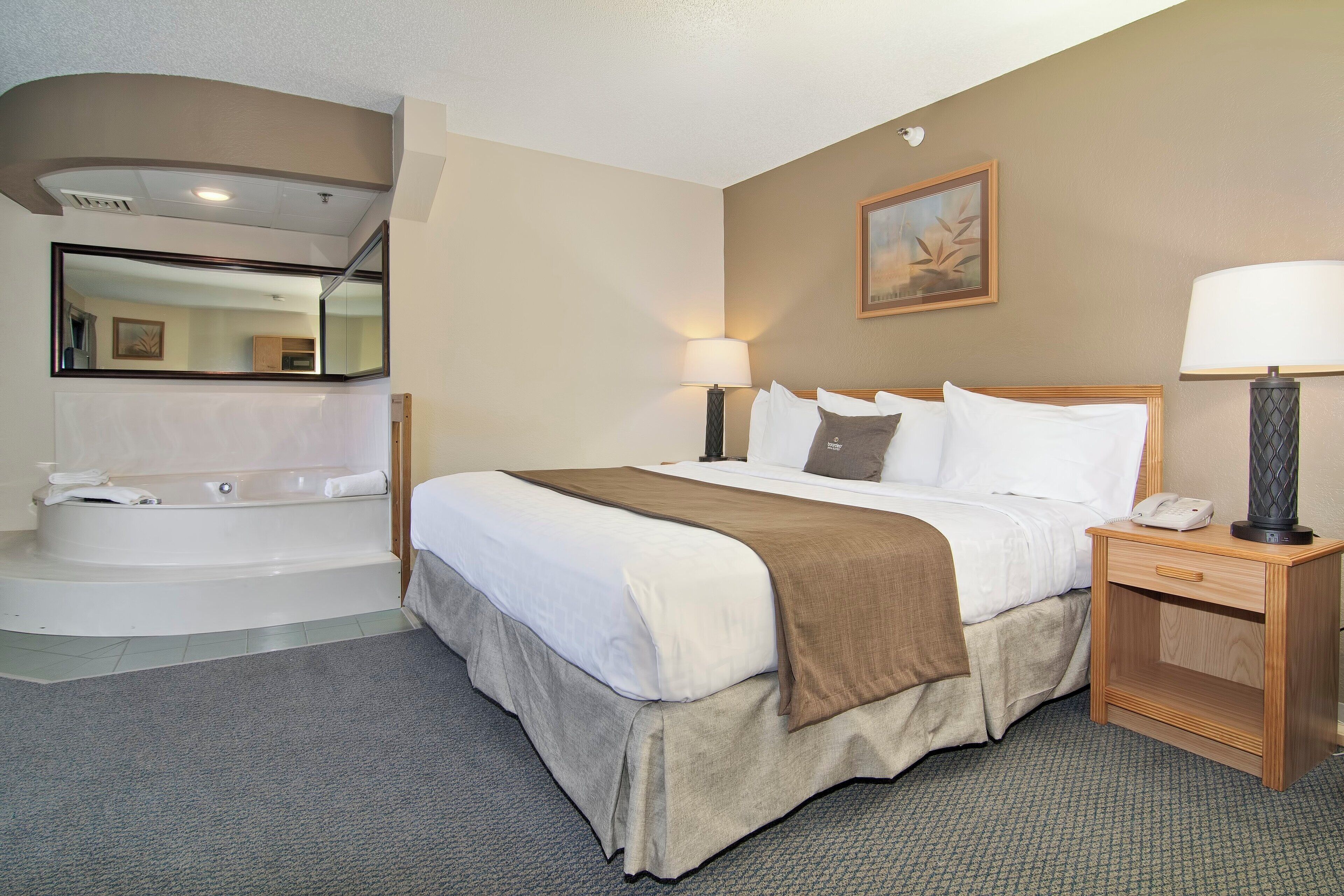 Habitación de hotel con una cama grande, un baño independiente con bañera, una mesita de noche con lámpara y un cuadro en la pared.