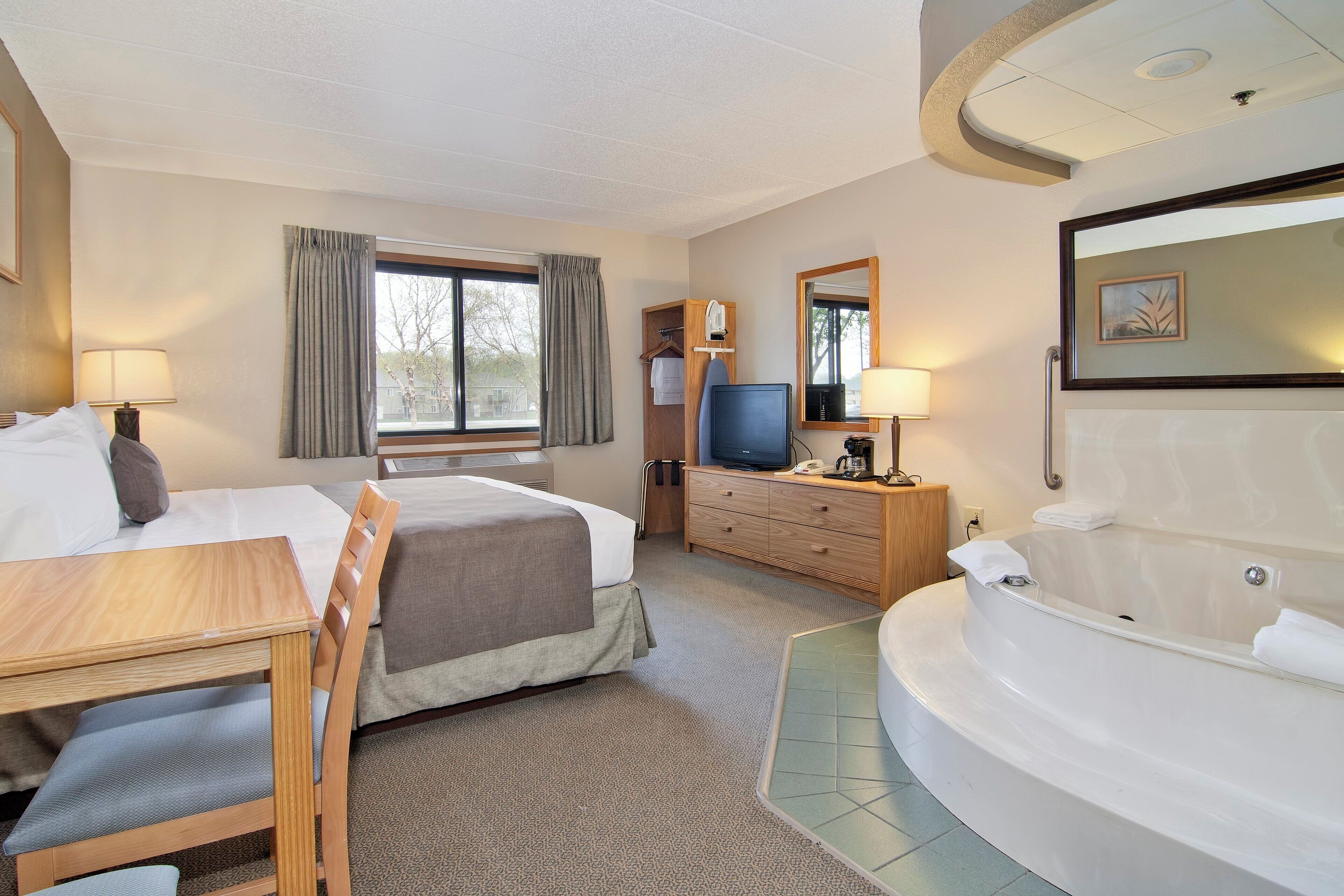 Habitación de hotel con dos camas, un escritorio, televisor, baño con bañera y ventana con cortinas.