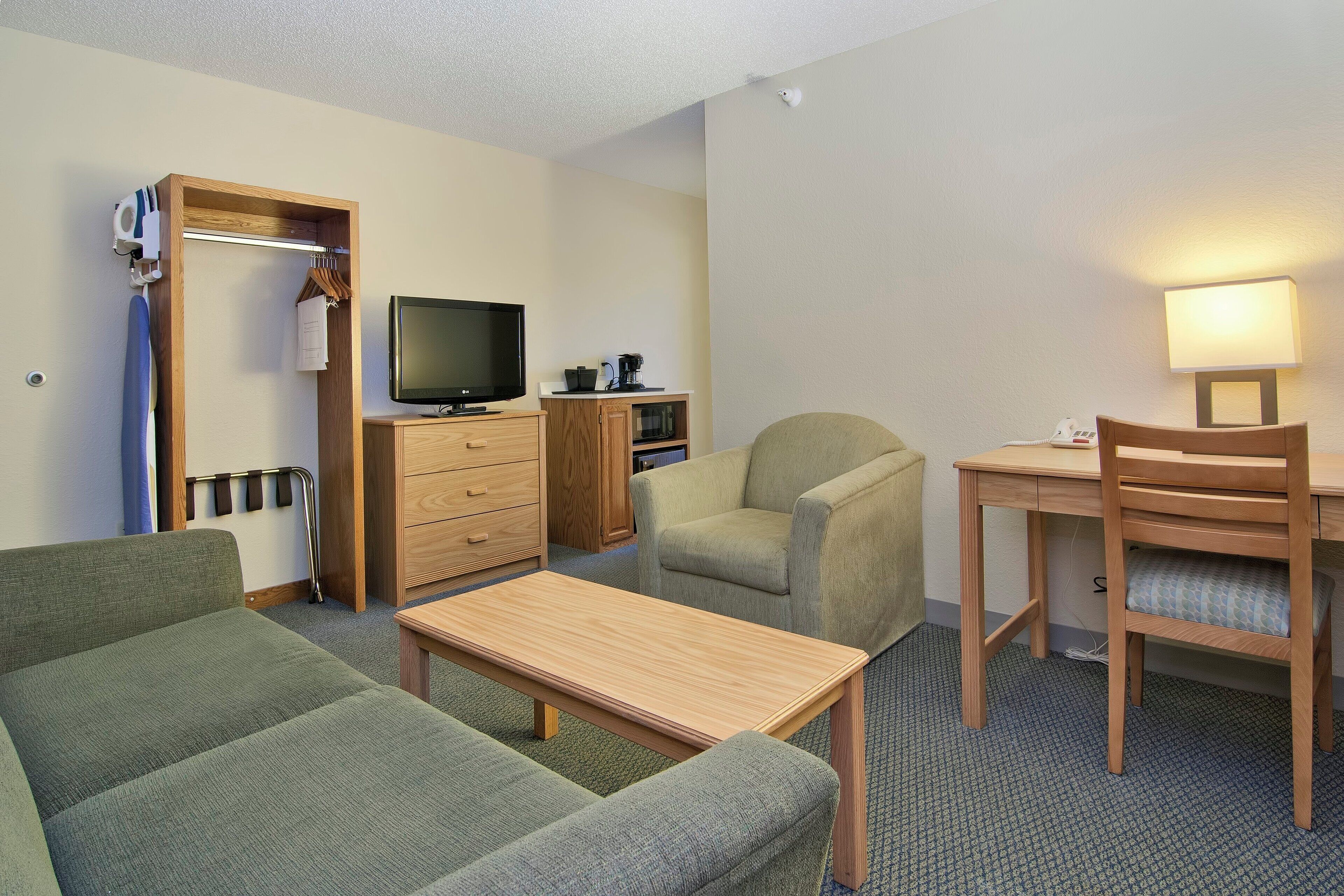 A hotel room with a green sofa, a wooden table, a TV, a lamp, and a wooden wardrobe.