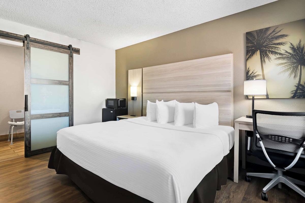 Een hotelkamer met een groot bed, een bureau met een computer, een stoel, een schuifdeur en een wandlamp.