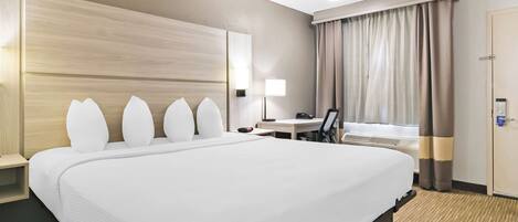 Habitación de hotel con una cama grande, un escritorio, una silla, una lámpara y un armario.